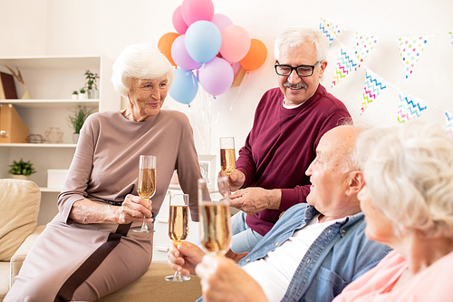 Several aged people with flutes of champagne enjoying home party and interacting
