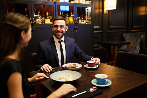 Cheerful young man talking to his girlfriend in luxurious restaurant while both having dessert