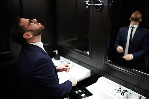 Young man in formalwear keeping his head shaken back while taking drugs by sink in lavatory
