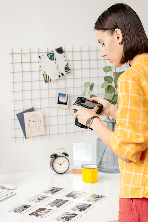 Young brunette photographer with photocamera standing by desk and shooting collection of photos for property release