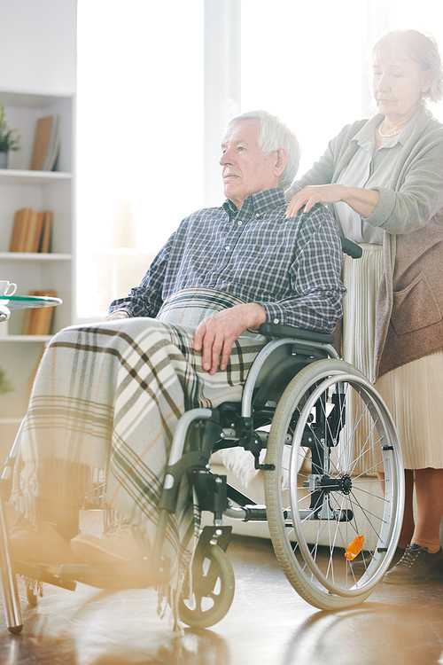aged disable man sitting in . with his wife or caregiver standing behind while spending time together