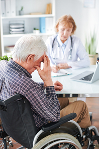 mature sick frustrated man in . sitting by desk in front of doctor making notes or medical prescriptions in document