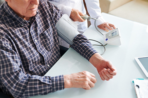 Overview of senior sick man having his blood pressure measured by doctor in hospital as a regular daily procedure