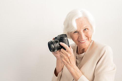 Successful senior female photographer with camera looking at you with toothy smile over white background in isolation