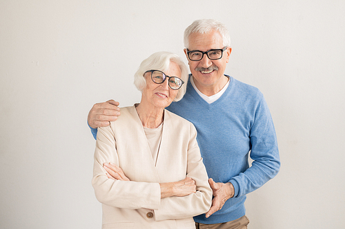 Senior affectionate couple in smart casualwear looking at you while standing in front of camera in isolation