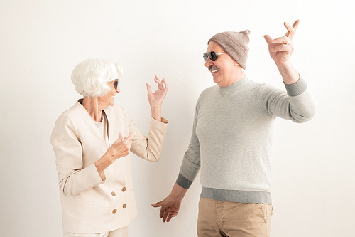 Happy senior couple in sunglasses and casualwear enjoying leisure while dancing over white background in studio