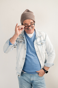 Happy mature man in casualwear standing on white background and looking at you through eyeglasses
