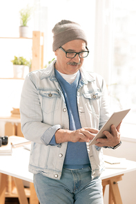 Casual mature businessman scrolling in touchpad while surfing in the net or looking through information