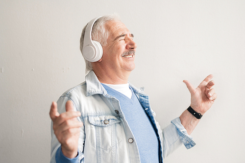 Cheerful senior man with headphones listening to his favorite music and enjoying it in isolation