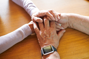 Hands of affectionate senior man and woman on wooden table symbolizing togetherness and love