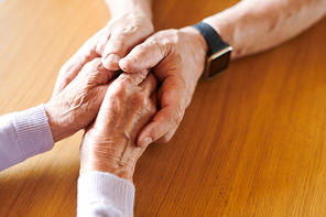 Hands of aged female in those of supportive husband comforting her in hard period of their family life