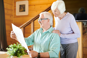 Happy mature man and his wife reading latest news in newspaper in the morning after breakfast