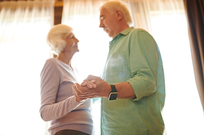 Hands of senior spouses looking at one another and talking during dance against window at home