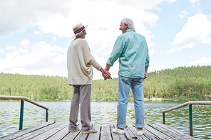 Happy amorous senior spouses in casualwear looking at one another while enjoying rest by waterside on summer day