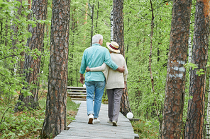 Rear view of amorous and affectionate senior husband and wife taking walk in the forest in embrace on summer day