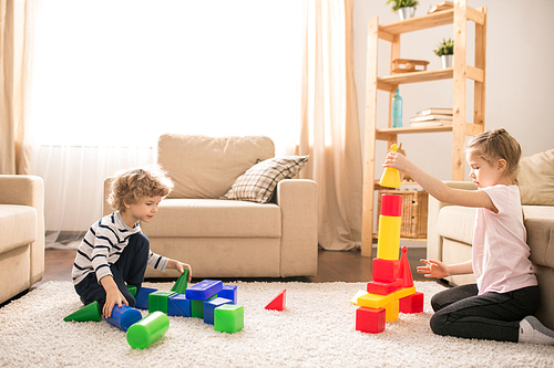 Little kids making toy towers on the carpet while playing on the floor of living room at home
