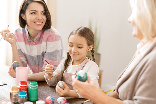 Happy young woman, her daughter and mother painting eggs for Easter with colorful gouache before holiday