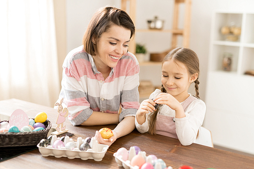 Young cheerful woman and her little daughter looking through painted Easter eggs and choosing one for grandmother