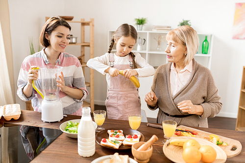 Little girl taking peel off banana while helping her mom and grandma with fruit smoothie for breakfast