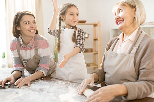 Happy cute little girl in apron standing between her mother and grandmother cooking dough and homemade pastry