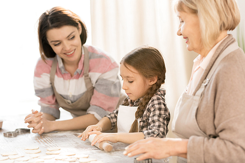 Little girl learning to roll dough and make homemade pastry or cookies with her mother and grandmother