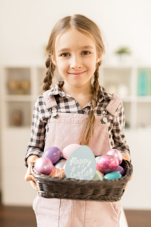 Happy little adorable girl with small basket of painted Easter eggs standing in front of camera