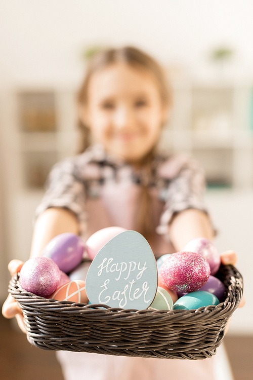 Basket full of painted Easter eggs and small greeting card held by little girl preparing for holiday