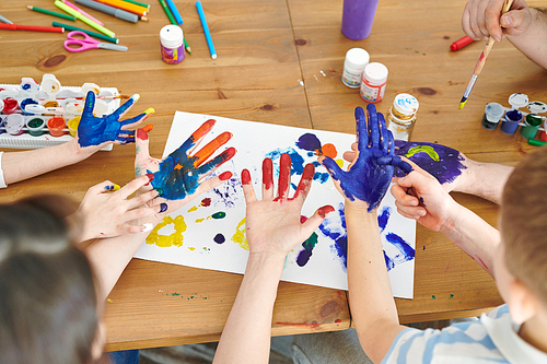 Young woman and her kids painting their hand palms with gouache to make prints on paper