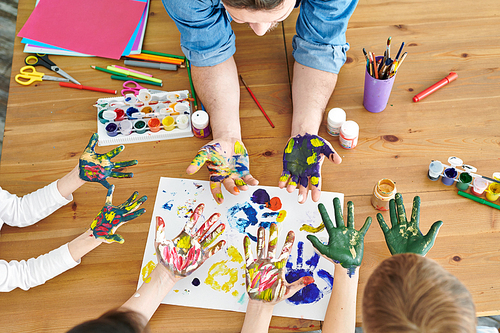 Overview of young family of four showing their hands in paint while sitting by table and making handprints