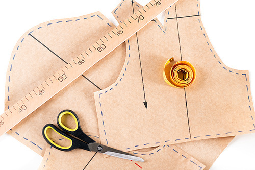 Overview of cut paper patterns, scissors, ruler and folded measuring tape on workplace of tailor