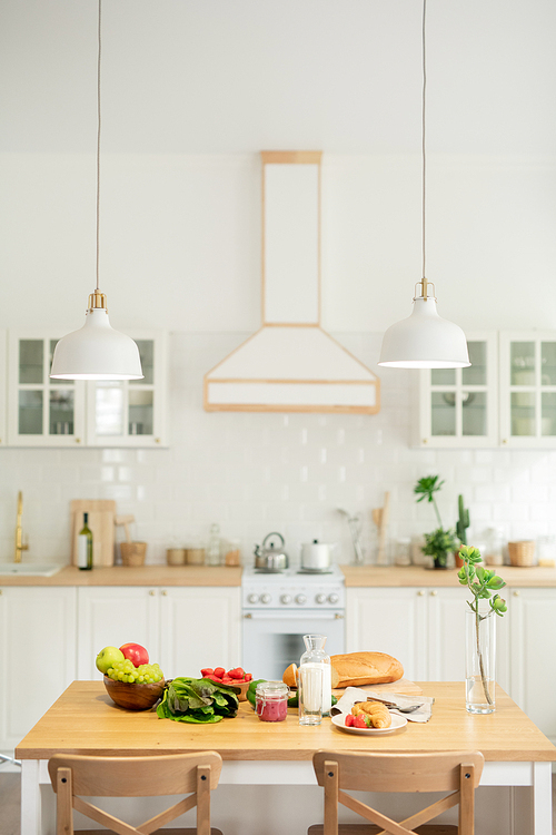 Interior of kitchen in modern flat or house with kitchenware and lamps hanging over table with vegetables and homemade food