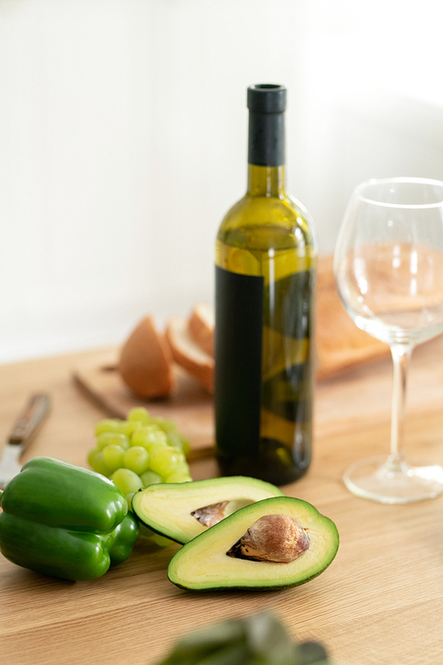 Fresh green fruits and vegetable, bottle of white wine and wineglass on wooden table on background of wheat bread