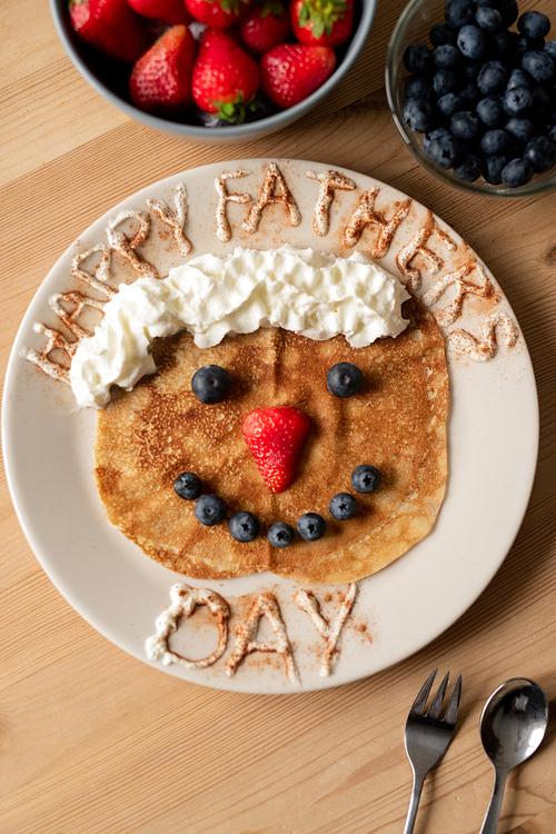 High angle view of funny crepe decorated with whipped cream and berries on plate, breakfast on fathers day