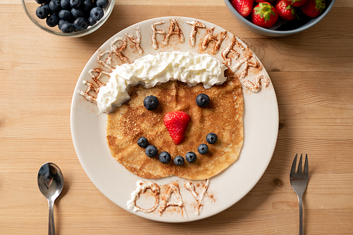 Sweet crepe decorated with whipped cream and berries in shape of funny face with happy fathers day inscription, gift for daddy