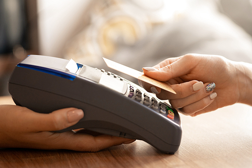 Hand of contemporary female holding plastic card over electronic payment machine while paying for what she bought or ate