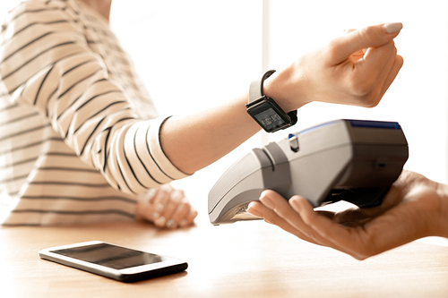 Arm of young modern woman with smartwatch on wrist keeping it over electronic machine while paying for goods or service