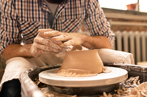 Contemporary young potter flattening bottom of new clay bowl with special handtool while bending over wheel