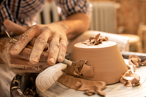 Master of pottery craft making sides of new clay bowl flat and smooth with special handtool during work