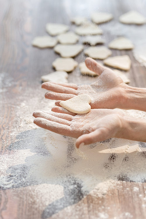 Hands of woman holding one of raw cookies in shape of heart while cooking homemade pastry