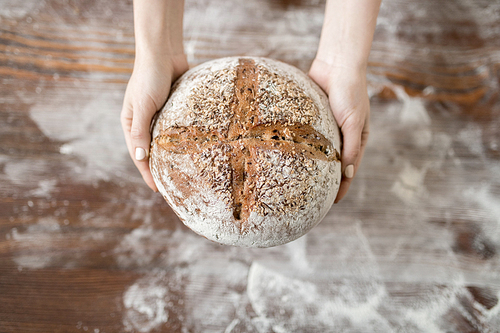 Overview of fresh rye homememade round bread held by female hands over table and flour