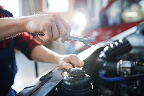 Hand of young repairman holding wrench over open engine of car during working process