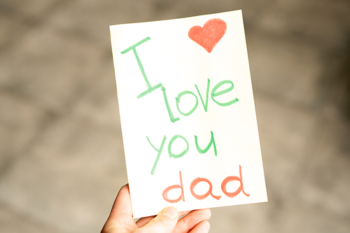Close-up of girl holding creative card with I love you Dad inscription and red heart in corner