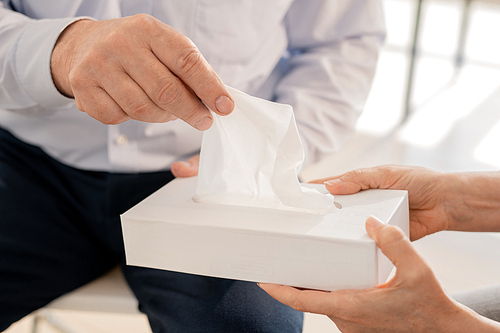Hand of senior man taking paper tissue from box being offered by groupmate or counselor