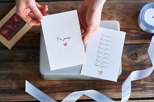 Top view of human hands holding handmade greeting card for valentine day over giftbox