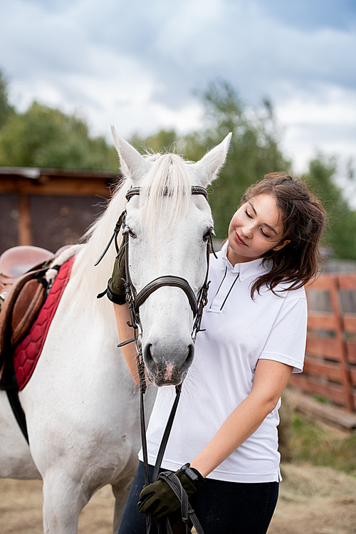 young woman cuddling white racehorse and looking at her while chilling out in rural