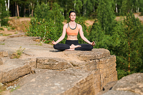 Content attractive flexible girl sitting with crossed legs and hands in mudra on knees, woman enjoying meditation in fresh air
