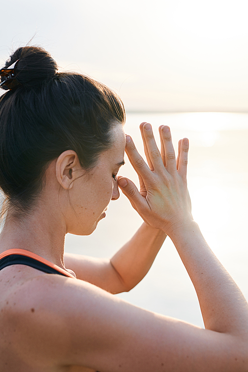 Serious young woman with hair bun focused on mind keeping eyes closed and leaning head on fingers outdoors