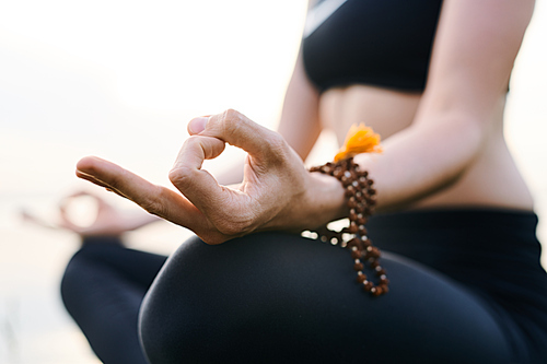 Close-up of unrecognizable woman concentrated on thoughts wearing mala beads on wrist meditating with hands in mudra