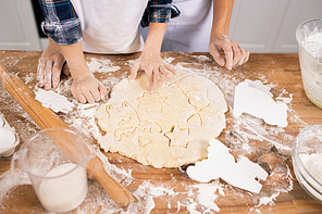 Hands of mother and son in white aprons cutting figures in rolled dough while making tasty cookies for holiday