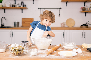 Cute and funny little boy pointing into bowl with flour while going to break egg to make dough for pastry